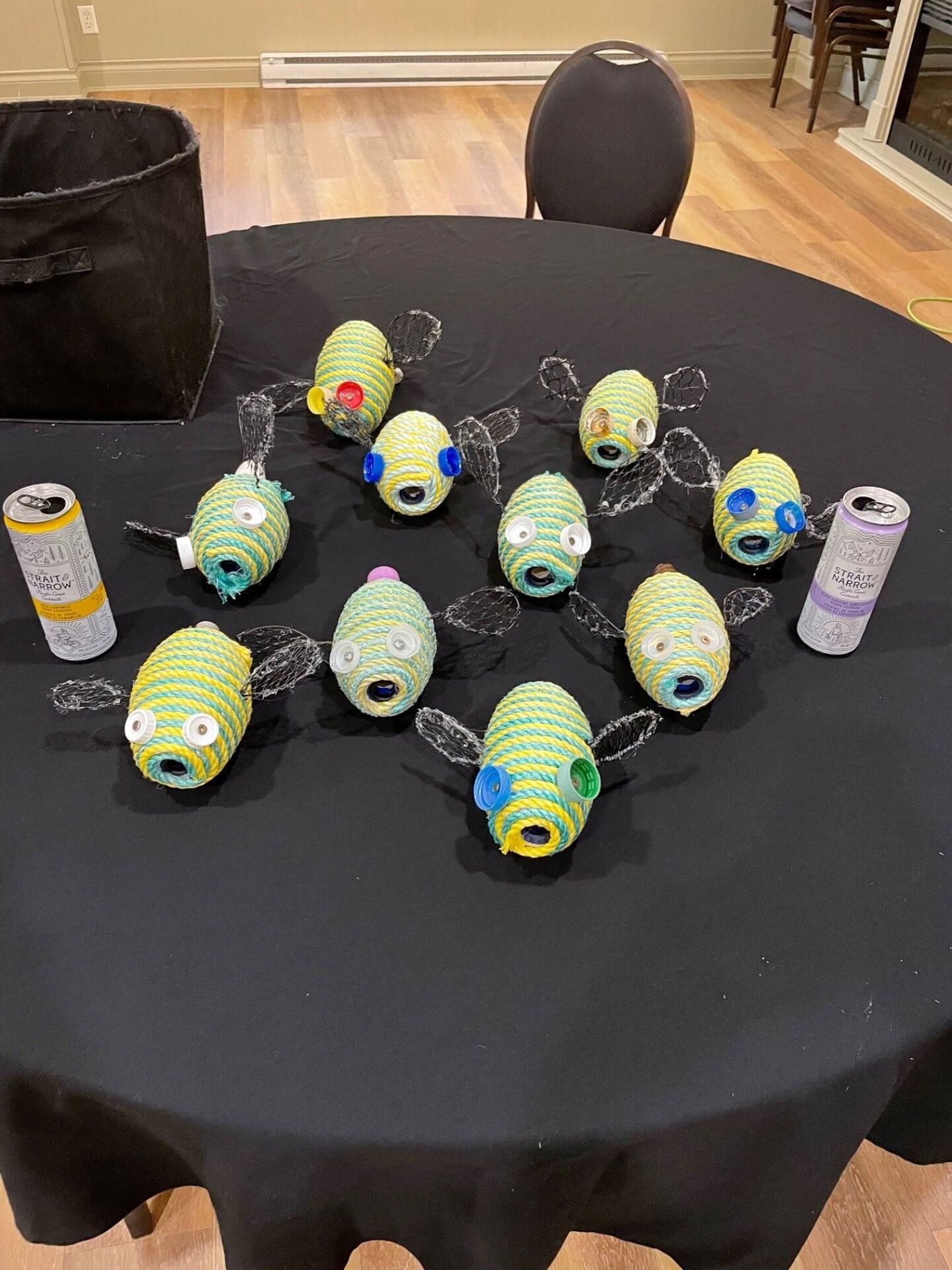 On an event table sits a swarm of yellow and blue-stripped bees made out of marine debris. The eyes are made from old bottle caps; the bees are made from while and netting; and stingers are made from a variety of discarded debris including forks and plast