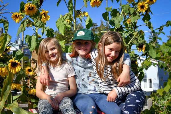 Children smiling and sitting in front of sunflowers at the Wickaninnish Community garden in Tofino