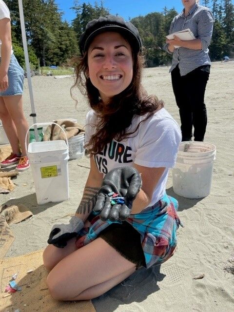 Kim Leckey kneels in the sand as she holds out her hand to show off the collection of marine debris she collected from Chesterman Beach during the Surf Rider Washed Up Wednesdays Beach Clean