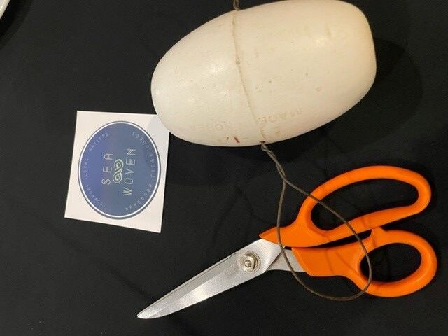 on an event table sits a pair of scissors, an old buoy and a sticker that reads "Sea Woven"