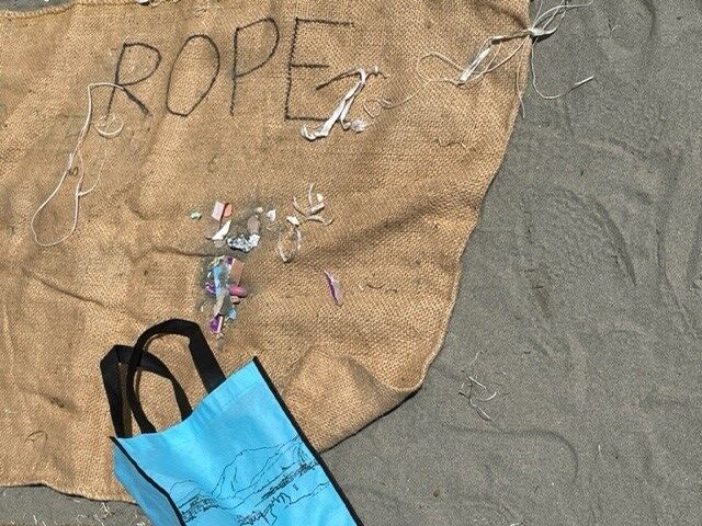 a bag labelled "rope" lies in the sand with pieces of plastic and other debris sits on top, ready to be sorted. 